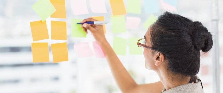 Smiling designer writing on sticky notes on window in creative office-1